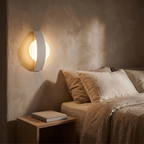 Acrylic wall lamp mounted beside a bed casting soft ambient light in a minimalist bedroom